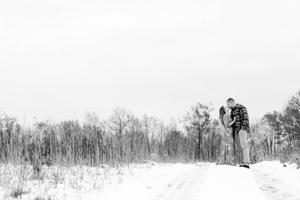 couple kissing in a black and white photo in a meadow that is snow covered for their winter engagement session in Ladysmith