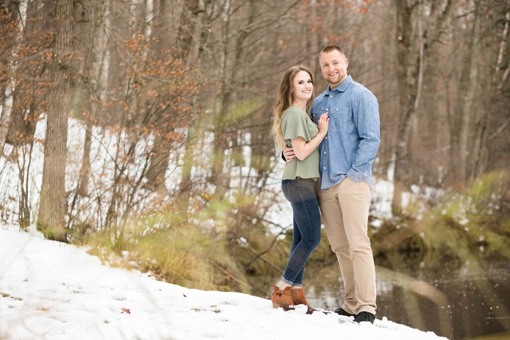 couple looking at the camera in a photo by the Chippewa River for their winter engagement session in Ladysmith