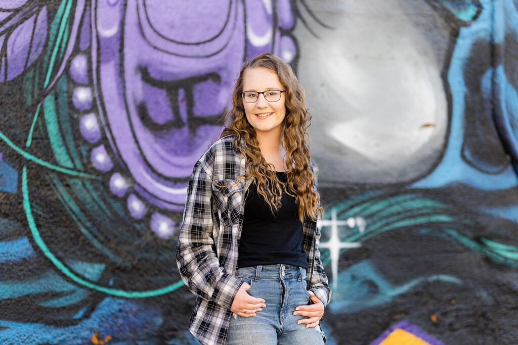 girl with a flannel shirt on infront of a graffiti wall mural in downtown eau claire for her senior photos